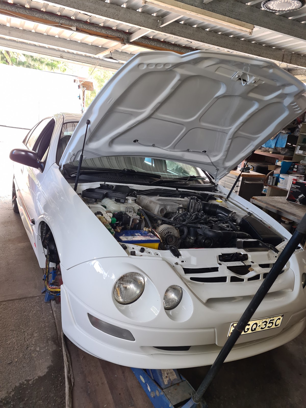 White sports car with the bonnet up in the workshop